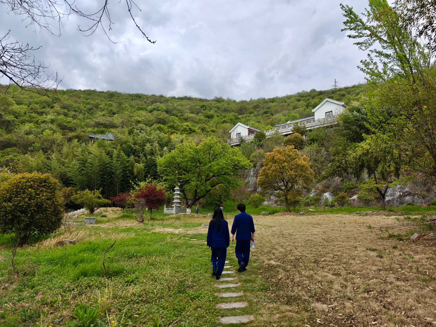 Two people in blue robes walking a stone path through the Anhui countryside